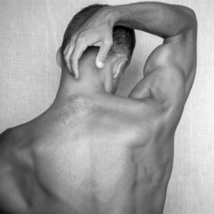 Back of young muscular man above gray background, black and white studio photo